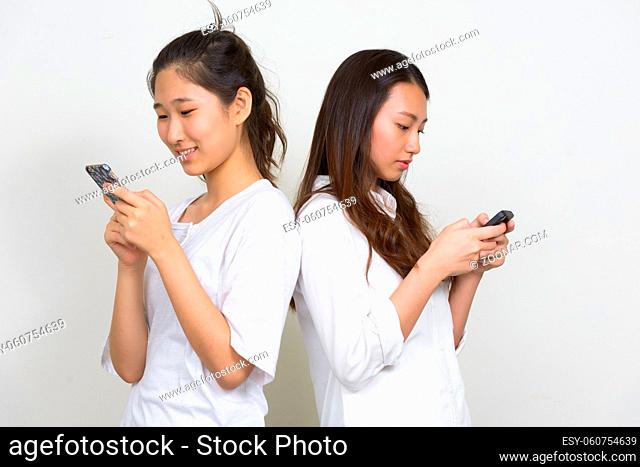Studio shot of two young beautiful Korean women as friends together against white background