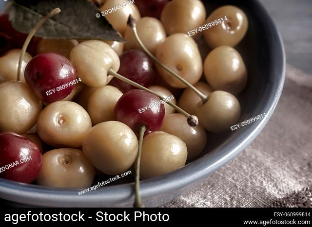 There are yellow and red cherries on the table in a ceramic cup. Front view, close-up