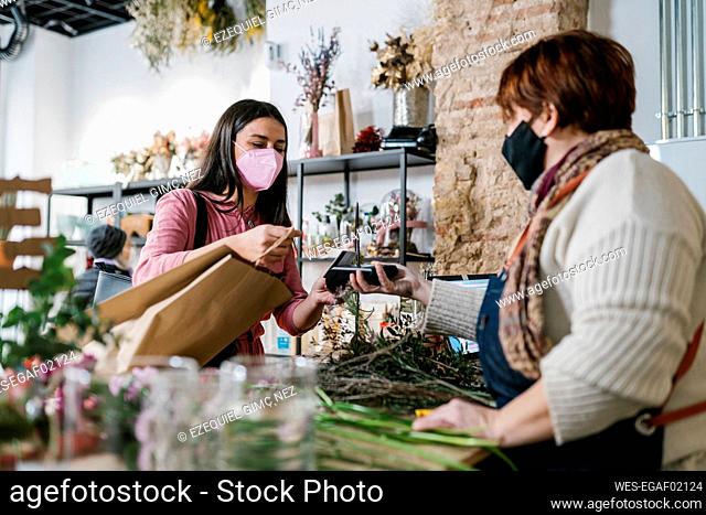 Female customer paying by credit card to florist at flower shop