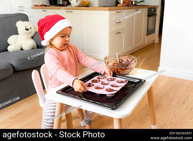 Child in santa hat preparing holiday cookies at home. Christmas activity at home for toddler . High quality photo