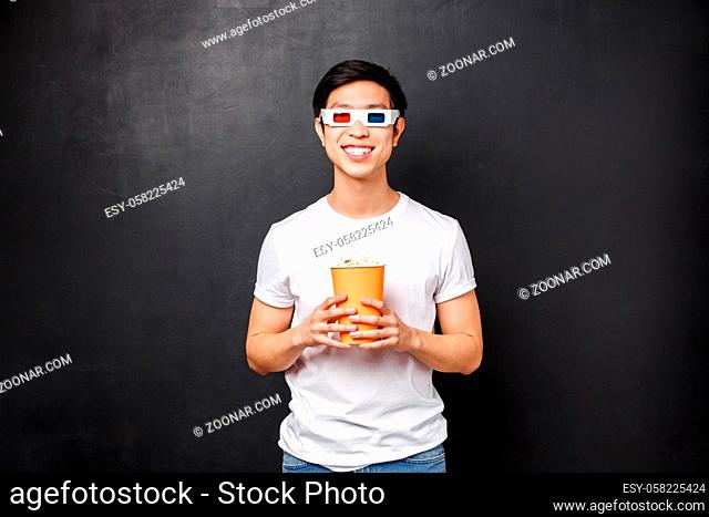 Leisure, movies and lifestyle concept. Handsome cheerful and excited asian man in 3d glasses, holding popcorn and smiling amused as watching favorite thriller...