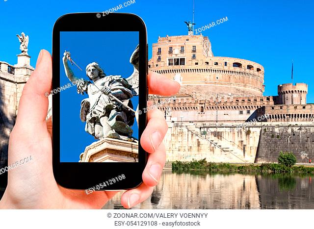 travel concept - tourist photographs figure of Michael the Archangel on top of Holy Angel Castle (Castel Sant Angelo) in Rome city on smartphone in Italy