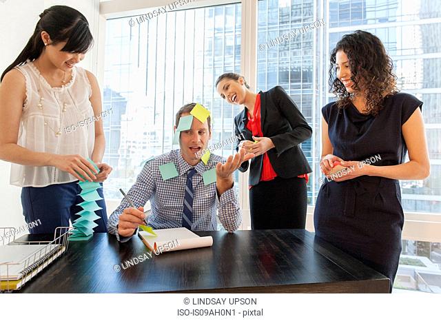 Female office workers covering male colleague with sticky notes