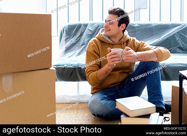 Smiling man with coffee cup looking away while unpacking in new home