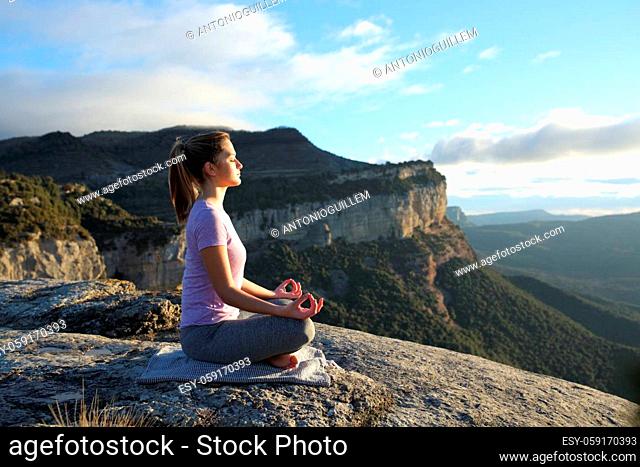 Profile of a woman doing yoga in the top of a cliff in the mountain