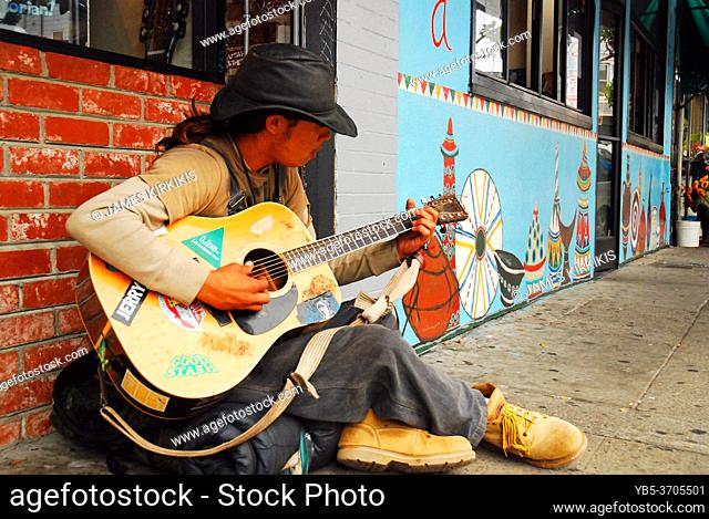 A young man strums his guitar for tips on the streets of the Haight Ashbury district of San Francisco