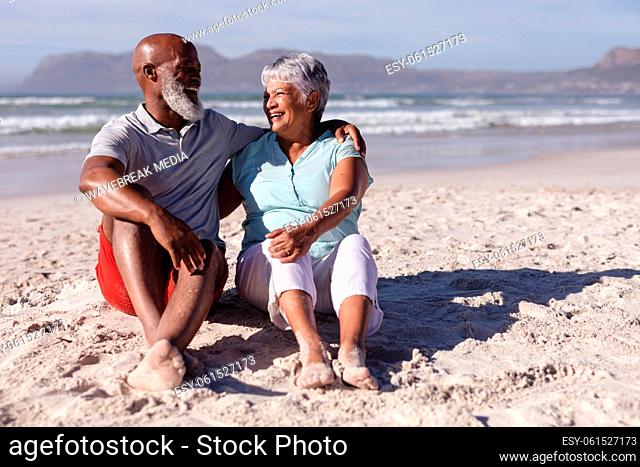 Senior african american couple smiling while looking at each other sitting on the beach