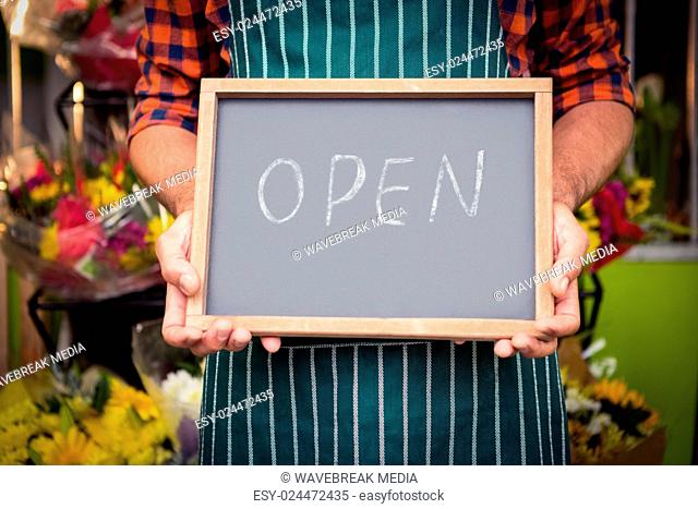 Male florist holding open sign on slate at his flower shop