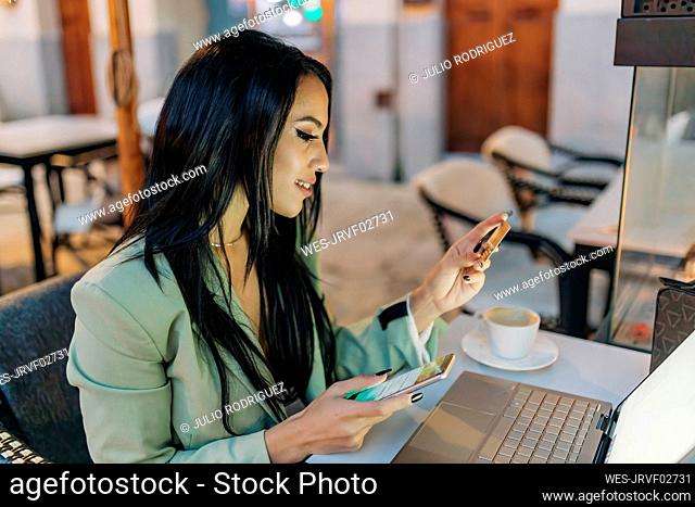 Businesswoman paying through credit card on smart phone at cafe