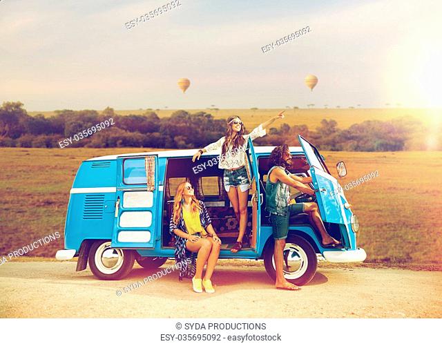 summer holidays, road trip, travel and people concept - smiling young hippie friends in minivan car over african savannah background