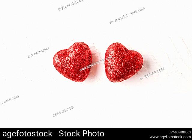 Two small glitter red hearts on a white wood background - love and valentines day concept
