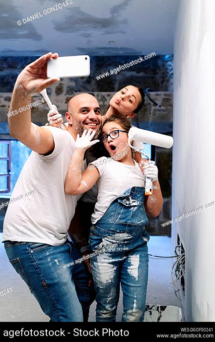 Happy family taking a selfie while painting the walls of her new house