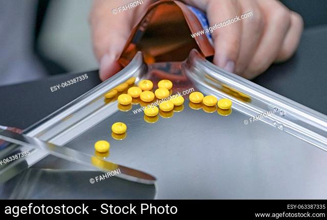 Selective focus on yellow tablets pills on stainless tray with blur hand of pharmacist or pharmacy technician counting pills into a plastic zipper bag