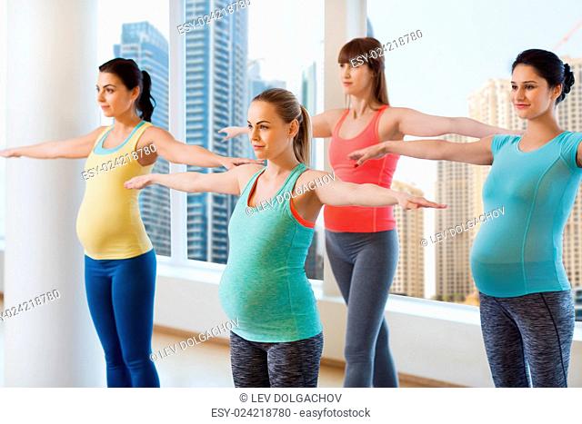pregnancy, sport, fitness, people and healthy lifestyle concept - group of happy pregnant women exercising in gym over city window view background