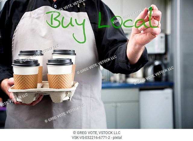 Man holding four cups of coffee and writing buy local on glass using sharpie