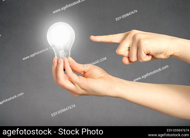 A finger pointing to a glowing light bulb in a hand