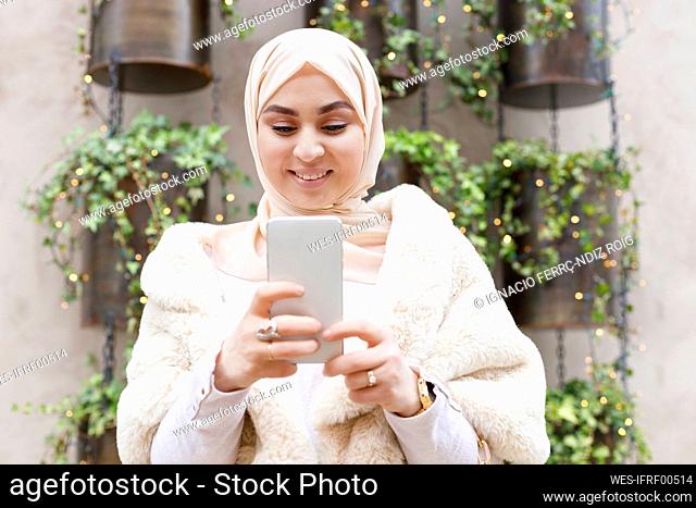 Smiling woman wearing hijab using mobile phone