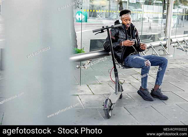 Man with smartphone and e-scooter at bus stop