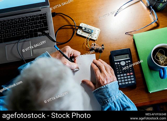 Cropped image of senior man making diagram on paper while repairing laptop at home