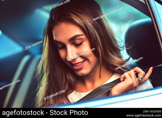 Beautiful woman with phone smiling while sitting on the back seat in the car