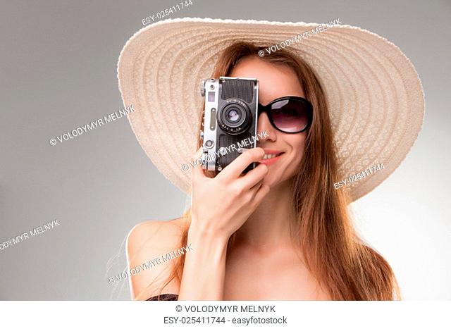 Girl in broad-brimmed hat and sunglasses with retro camera isolated on gray background
