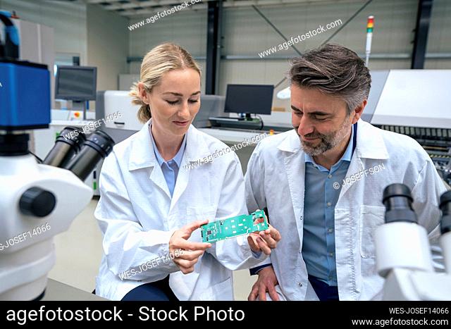 Smiling scientists examining circuit board sitting in industry