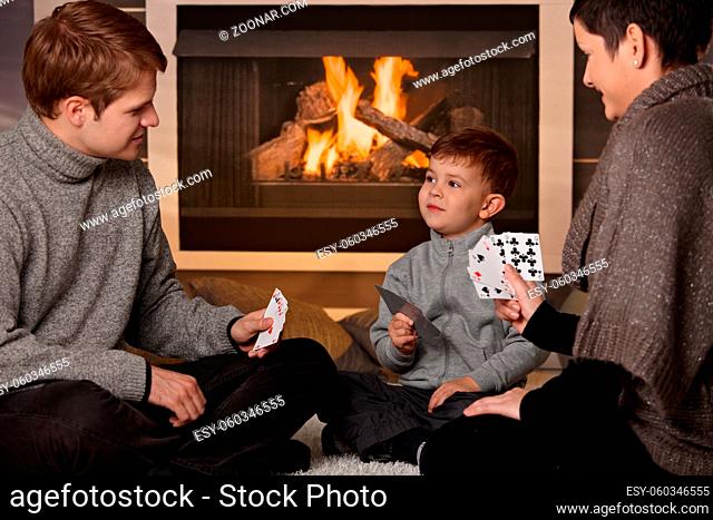Young family with 4 years old kid playing card game at home in a cold winter day