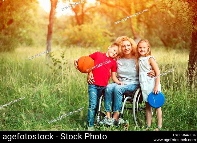 Blonde Woman In A Wheelchair With Her Two Kids - Young Son And Beautiful Daughter Smile At Camera. Outdoor