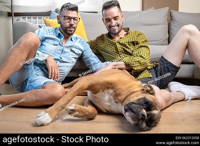 Happy gay couple sitting on floor and playing with dog at home. High quality photography