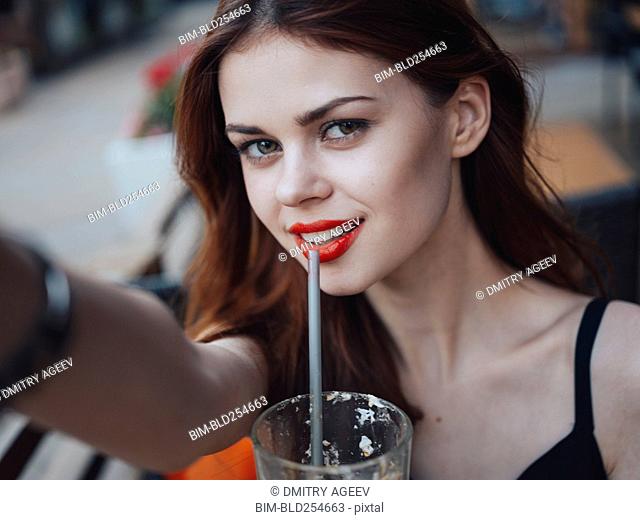 Smiling Caucasian woman drinking from straw posing for selfie