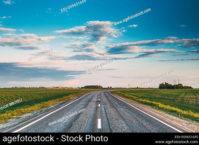 Curved Asphalt Country Open Road Through Spring Fields And Meadows In Sunny Evening. Landscape In Belarus Or European Part Of Russia In Early Summer Season At...