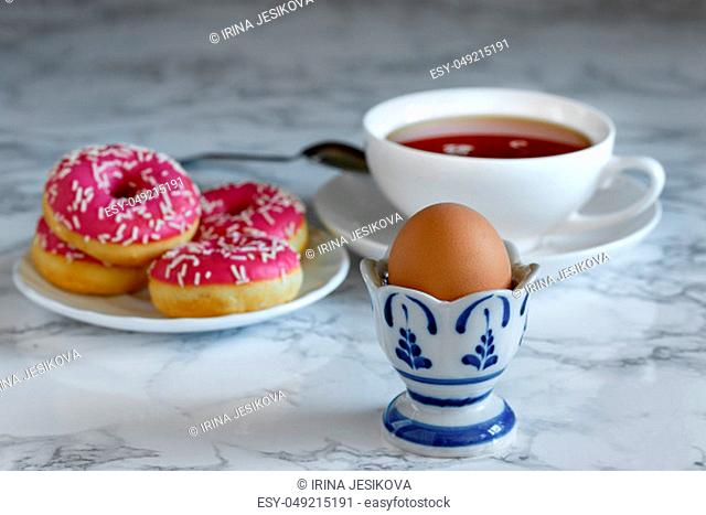 Boiled egg with tea and donuts in the background, breakfast time