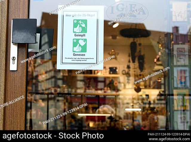 24 November 2021, Brandenburg, Lübbenau: A sign that reads ""2G Rule Vaccinated Get Well Here"" hangs behind the glass of the front door to a downtown store