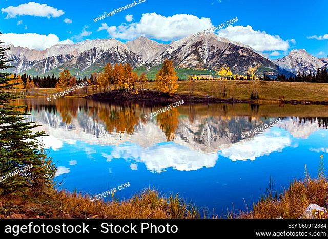 Outskirts of Kenmore. Three Sisters Mountain in Canadian Banff Park. Bright autumn forest is reflected in the smooth water of the lake