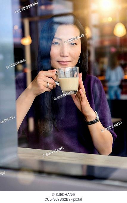 Mid adult woman with coffee looking out from cafe window seat, portrait