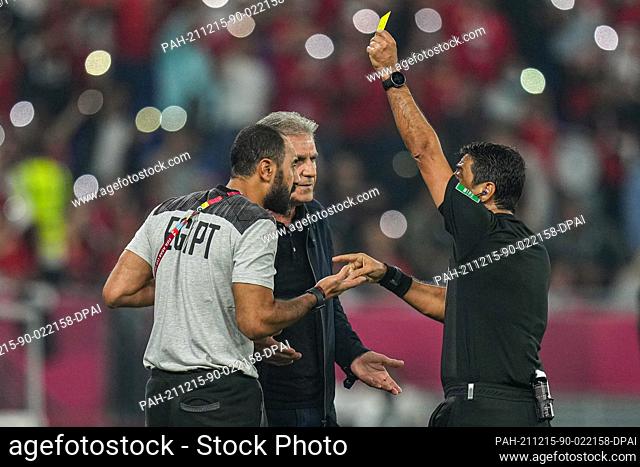 15 December 2021, Qatar, Doha: Egypt's head coach Carlos Queiroz (C) reacts as assistant coach Mohamed Shawky (L) receives a yellow card from referee Alireza...