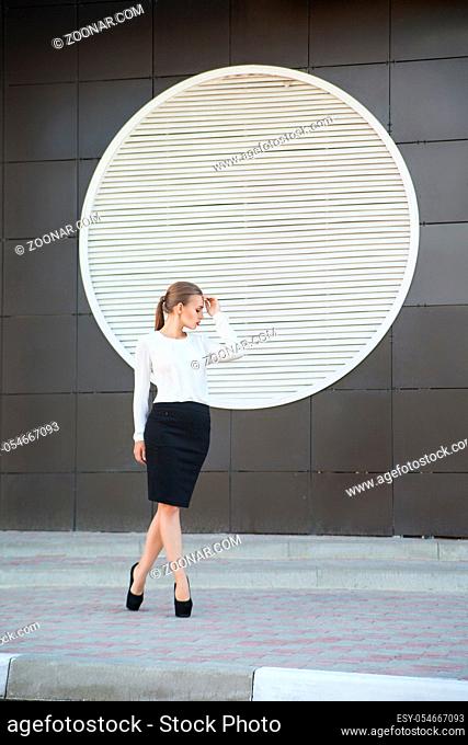 Businesswoman in stylish clothes looking down while posing against of white round ventilation wall