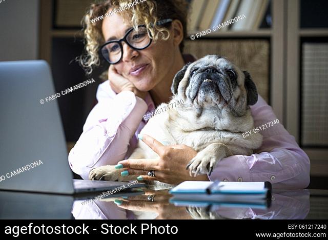 One woman portrait working at home on computer - cute puppy dog sitting together - modern people and new job lifestyle - adult female smile and watch laptop...
