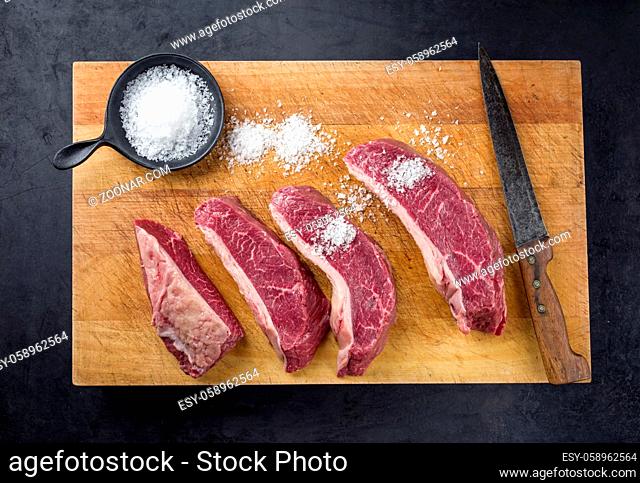 Raw dry aged wagyu cap of rump beef sliced for picanha barbecue skewer with salt offered as top view on a wooden rustic cutting board