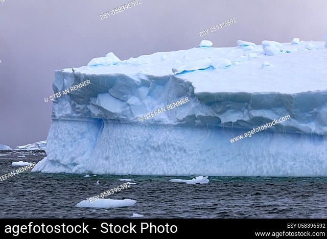 Detail of huge iceberg with icicles glows blue against beautiful background and play of colors