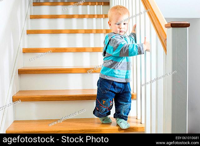 Toddler boy in dangerous situation at home, walking down the stairs. Teaching kids to use stairs properly. Child safety concept
