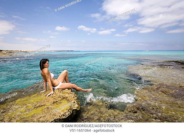 Young woman in bikini sitting on the rocks and enjoying the sea in Formentera, Spain