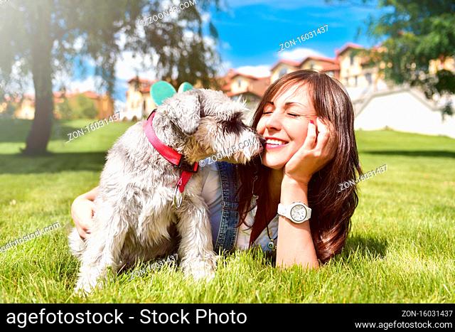 Pretty adult caucasian happy woman resting in the park on a sunny day with her beloved dog. Female lay on the grass smiling and looking at the camera