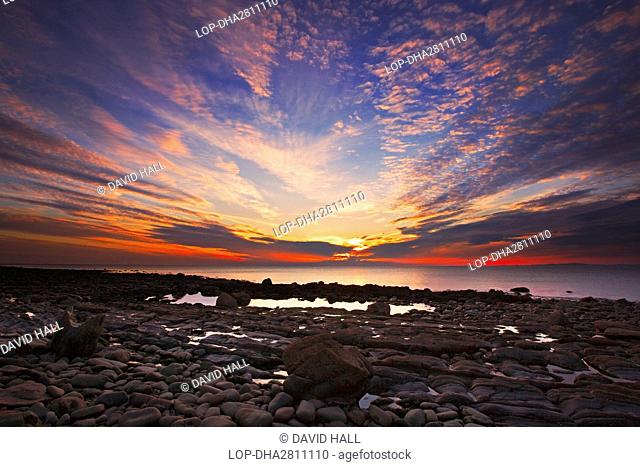Wales, Gwynedd, near Llwyngwril. View over rocks and pebbles on a beach near Llwyngwril towards a beautiful sunset after a storm
