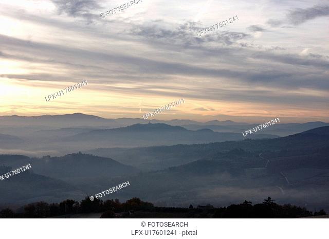 Sunrise over Tiber valley with grey pink and golden sky in the early morning mist of winter, with tree outline in foreground