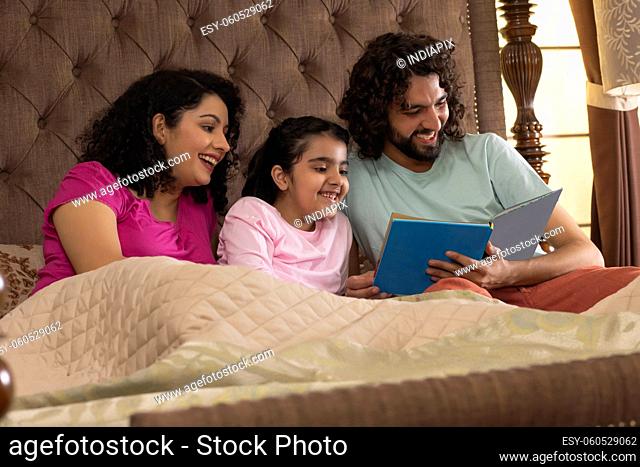 Happy family members watching photo album together in bedroom