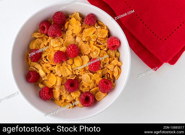 Breakfast cereal of cornflakes and raspberries on white background