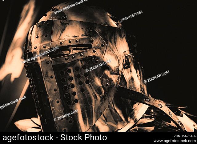 Shiny medieval iron knight helmet with a cross, full of scratches due to battles. In sepia