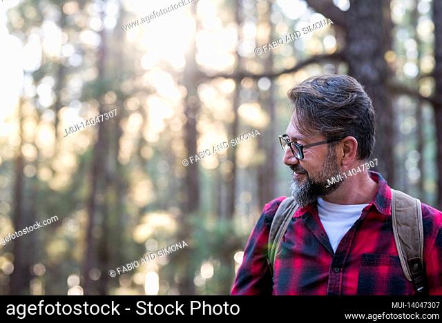 man hiking and enjoying in a woods forest location. side view of a man wearing a bag walking through a forest. happy adult young caucasian male portrait...