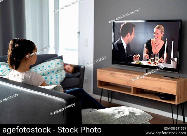 Woman Watching TV At Sofa While Child Is Sleeping